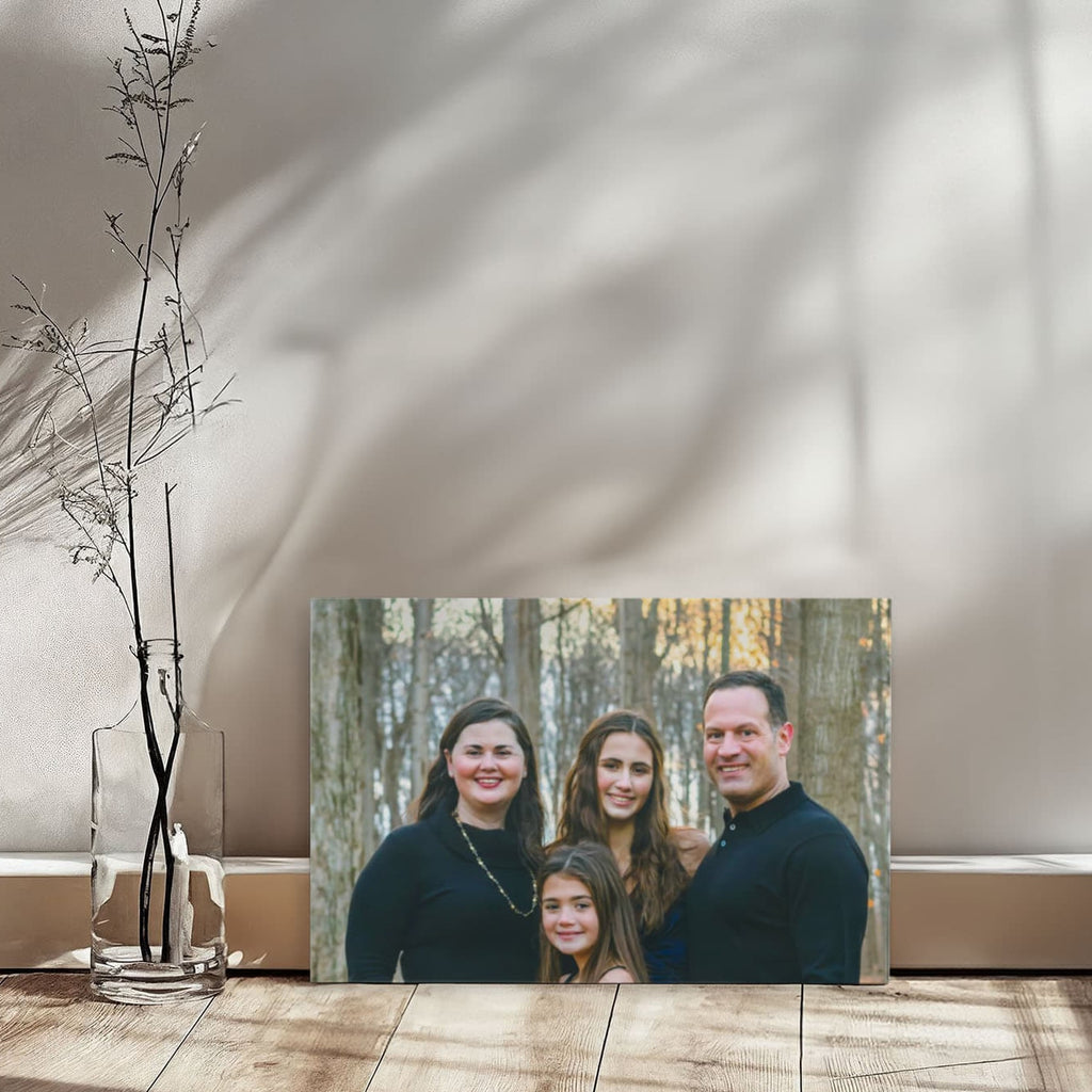 Family portrait canvas leaning against a sunlit white wall on a wooden floor, with window shadows and a slim vase of bare branches.
