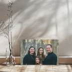 Family portrait canvas leaning against a sunlit white wall on a wooden floor, with window shadows and a slim vase of bare branches.