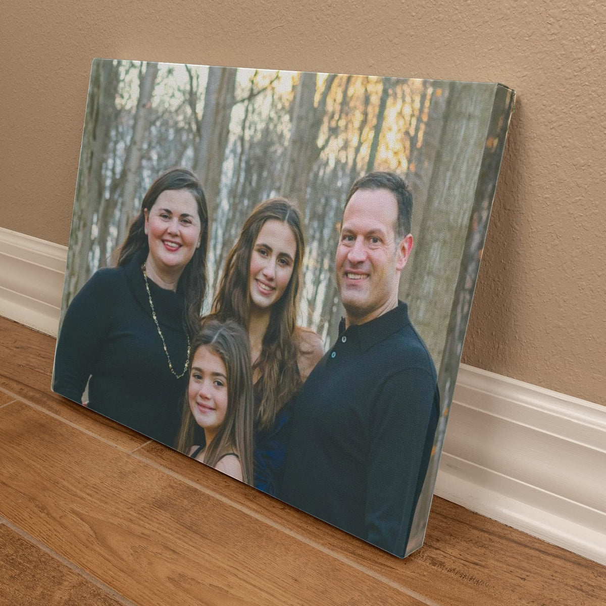 Angled view of the family photo canvas resting on a wood floor against a baseboard, showing the photo wrapping around the side of the canvas.