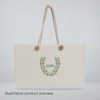 Video of a cream rope-handle weekender bag with a leaf wreath and AMH monogram, shown close-up and on a wooden table.