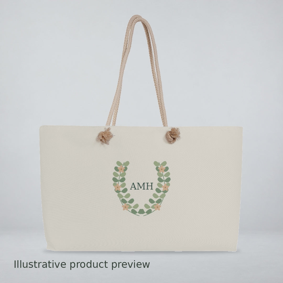 Video of a cream rope-handle weekender bag with a leaf wreath and AMH monogram, shown close-up and on a wooden table.