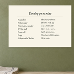 Sunday pancakes recipe canvas hanging on an olive kitchen wall above a cream counter.
